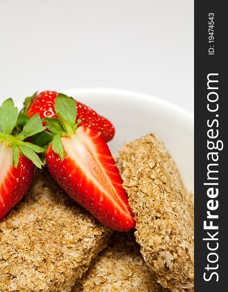 Sliced strawberries and wheat biscuits in a bowl.