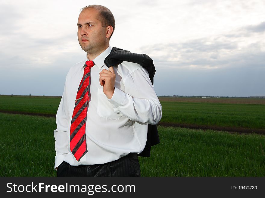 The young businessman costs in an open country having control over a jacket and looks in a distance. The young businessman costs in an open country having control over a jacket and looks in a distance