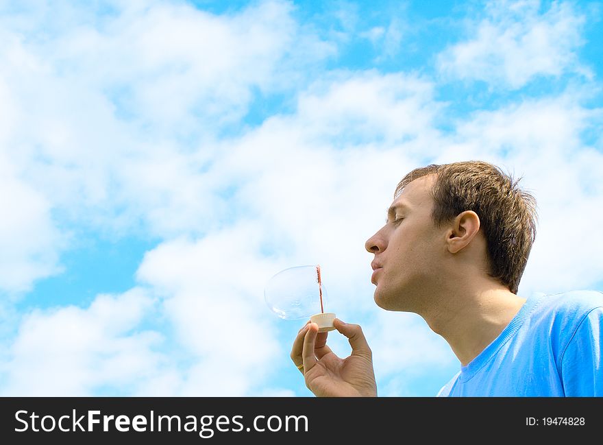 The young man starts up soap bubbles against the blue sky