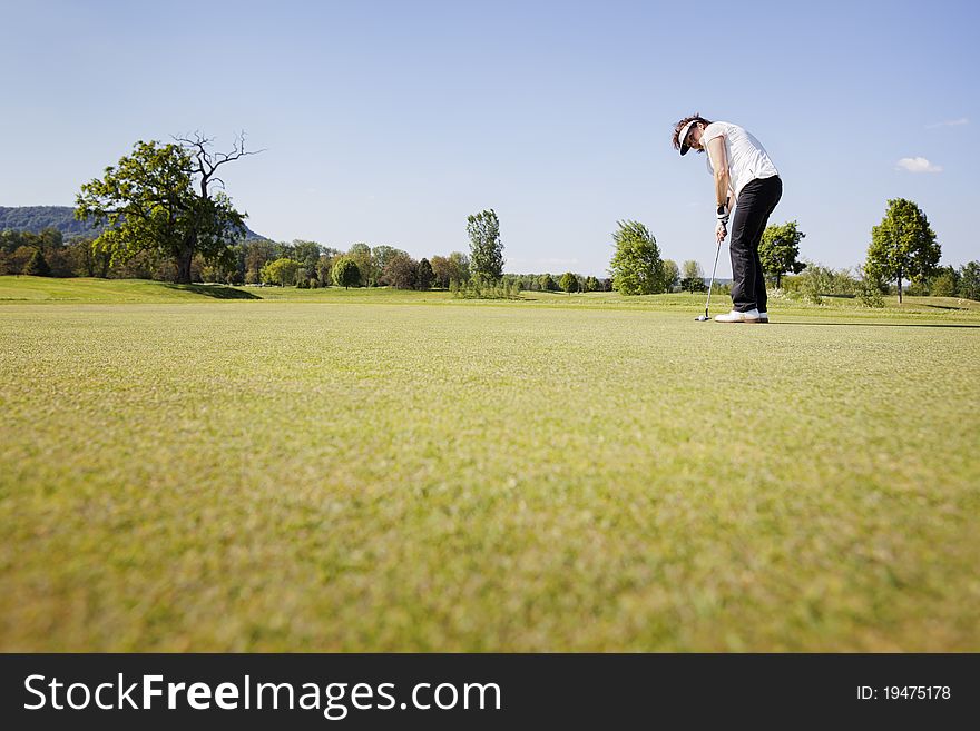 Active senior female golf player focusing for putting golf ball on green on beautiful golf course with blue sky in background. Active senior female golf player focusing for putting golf ball on green on beautiful golf course with blue sky in background.