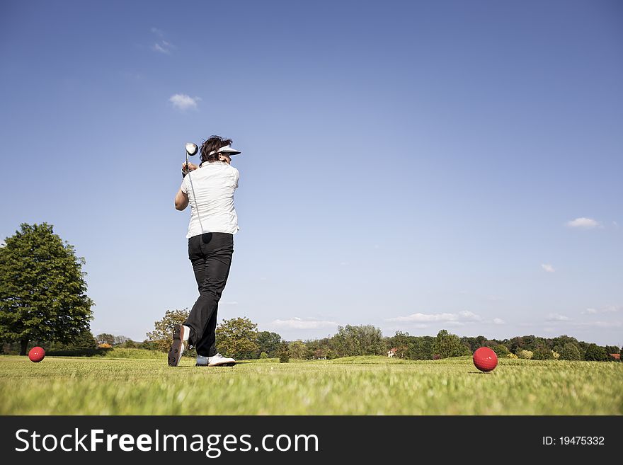 Active senior female golf player swinging golf club to tee off ball on beautiful golf course with blue sky in background. Active senior female golf player swinging golf club to tee off ball on beautiful golf course with blue sky in background.