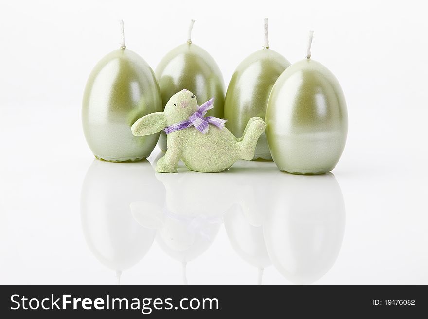 A green easter-bunny and four easter-candles on white background