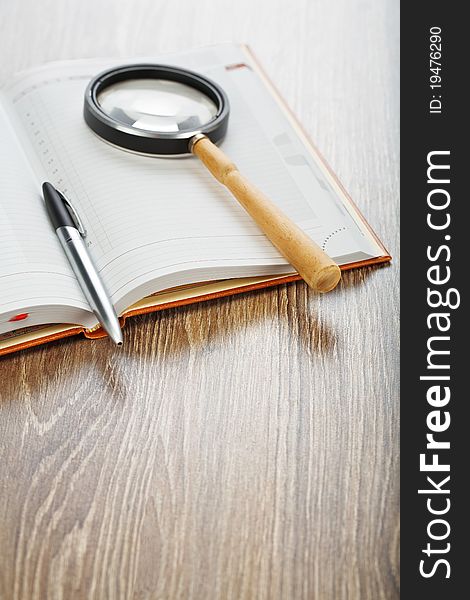 Studio shot composition of office or education accessories pen and magnifying glass on notebook on wooden board