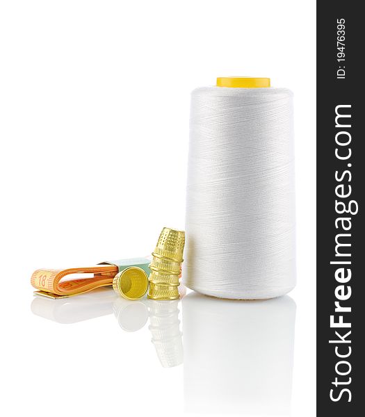 Studio shot sewing composition spool with white thread measuring tape an yellow timbles isolated on white background. Studio shot sewing composition spool with white thread measuring tape an yellow timbles isolated on white background