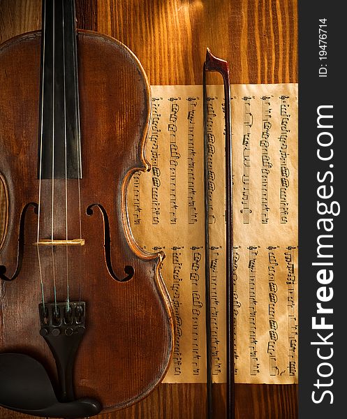 View on the violin and old musical note with fidlestick on old brown wooden board. View on the violin and old musical note with fidlestick on old brown wooden board