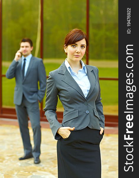 Businessman posing in front of business building and businesswoman in the background talking on the phone. Businessman posing in front of business building and businesswoman in the background talking on the phone