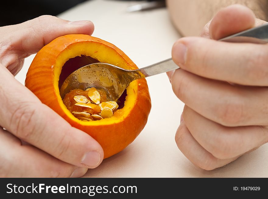 Man's hands using a spoon to hollow out a mini pumpkin. Man's hands using a spoon to hollow out a mini pumpkin