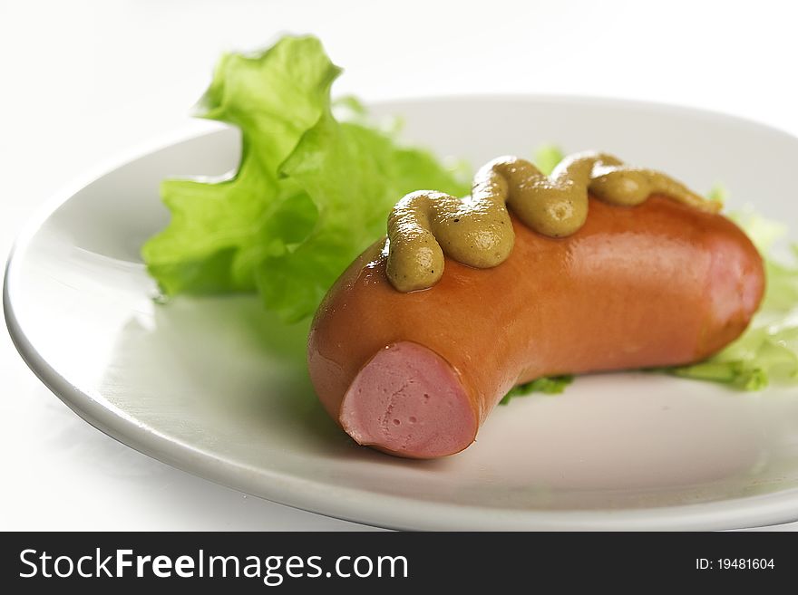 Small sausage with mustard and lettuce on the plate
