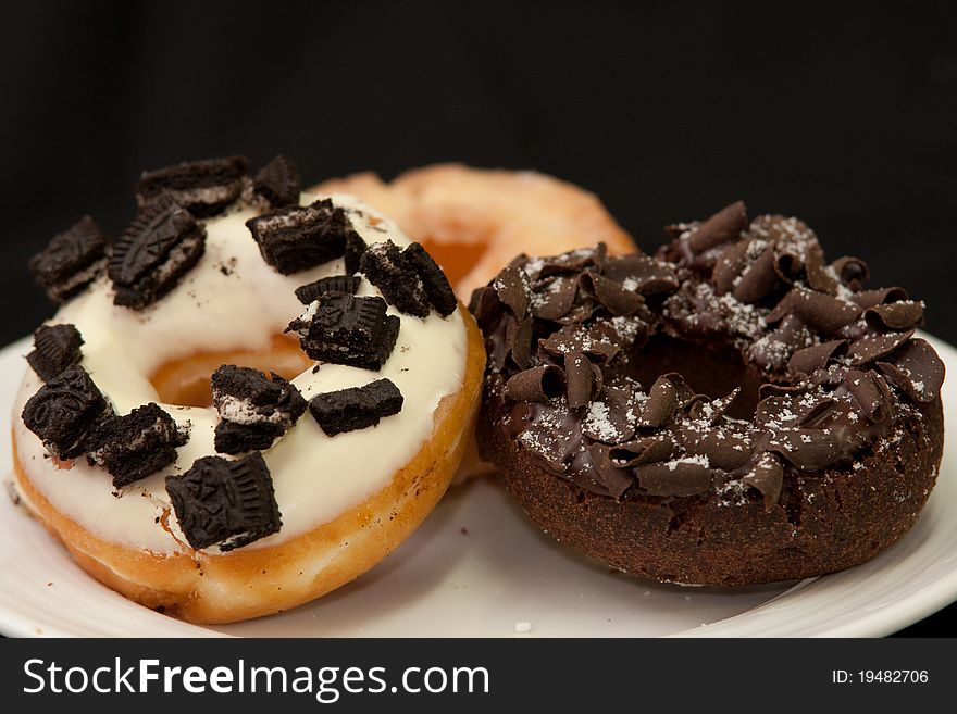 The white chocolate topping with olio and chocolate donut in white dish and dark isolated backgrond. The white chocolate topping with olio and chocolate donut in white dish and dark isolated backgrond