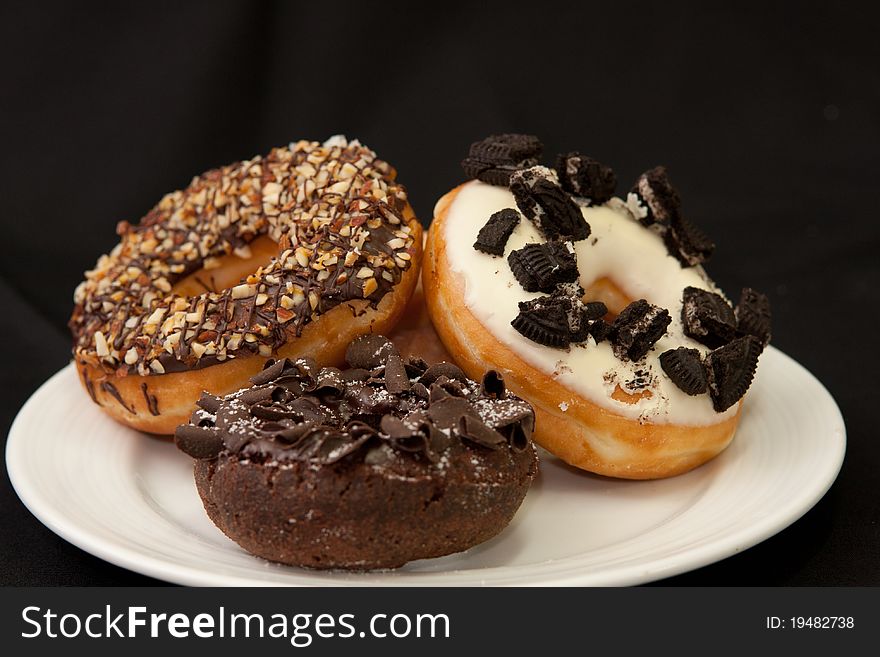 The white chocolate topping with olio and chocolate donut in white dish and dark isolated backgrond. The white chocolate topping with olio and chocolate donut in white dish and dark isolated backgrond