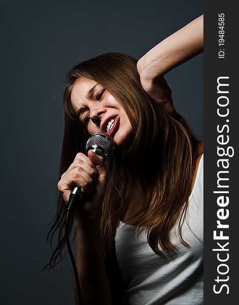 Young cute girl singing with microphone against a dark gray background. Young cute girl singing with microphone against a dark gray background