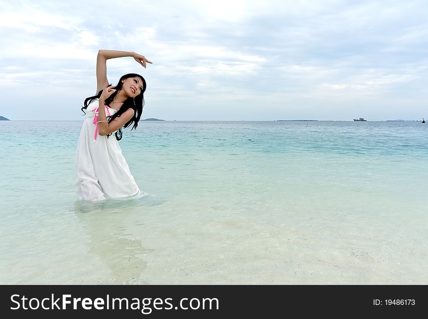 Young woman performs with raised hands on clear crystal beach of tropical island during holiday. Young woman performs with raised hands on clear crystal beach of tropical island during holiday