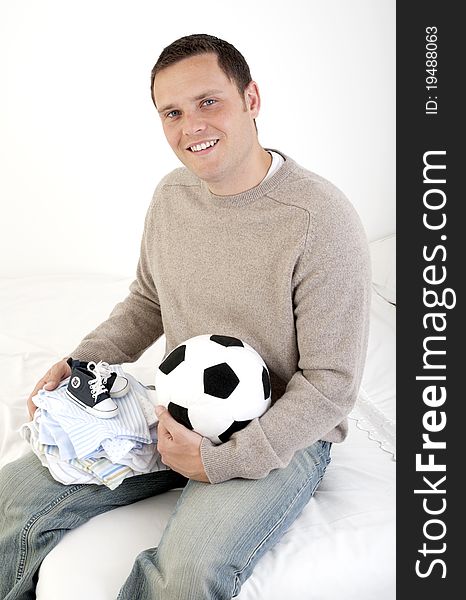 Man looking to camera holding baby boy clothes and football - baby son. Man looking to camera holding baby boy clothes and football - baby son