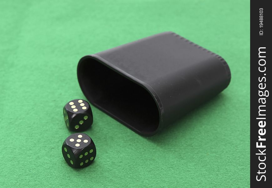 A dice with dice cup on a games green table.