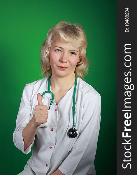 The woman the doctor, the blonde, average years, with a stethoscope shows a hand thumb upwards and smiles. The woman the doctor, the blonde, average years, with a stethoscope shows a hand thumb upwards and smiles
