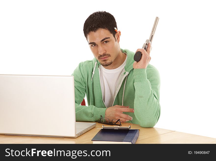 A man in green sitting at his table sick of studying by holding a gun and looking not happy. A man in green sitting at his table sick of studying by holding a gun and looking not happy.