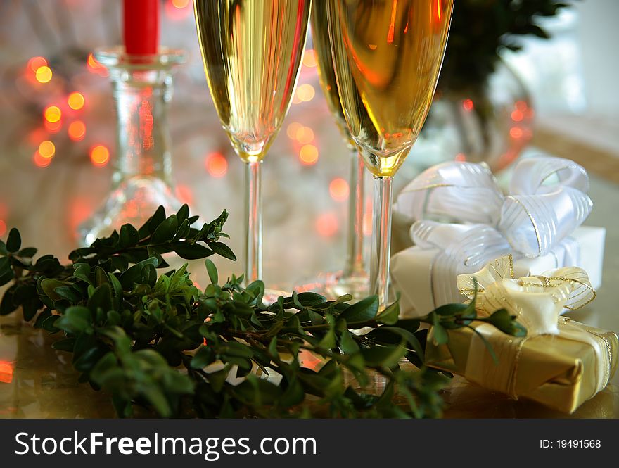 Champagne in glasses, green twig, gift boxes and blured lights on background. Champagne in glasses, green twig, gift boxes and blured lights on background.