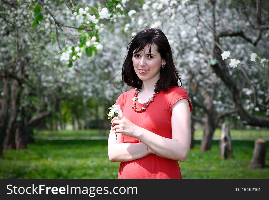 Girl in a red dress with a sprig of apple in his hands against the backdrop of flowering trees