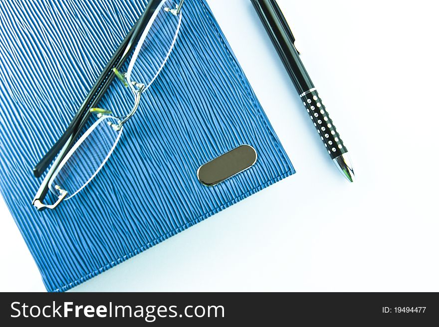 Glasses on blue notebook with black pen in isolation. Glasses on blue notebook with black pen in isolation