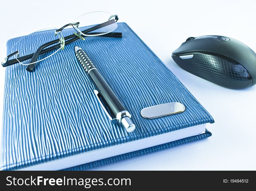 Glasses on blue notebook with black pen and mouse in isolation. Glasses on blue notebook with black pen and mouse in isolation