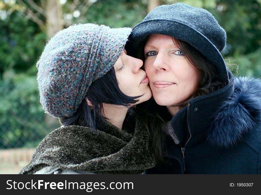 Mother and daughter, outdoor, warm clothes ,  closed together, close-up, giving a kiss. Mother and daughter, outdoor, warm clothes ,  closed together, close-up, giving a kiss