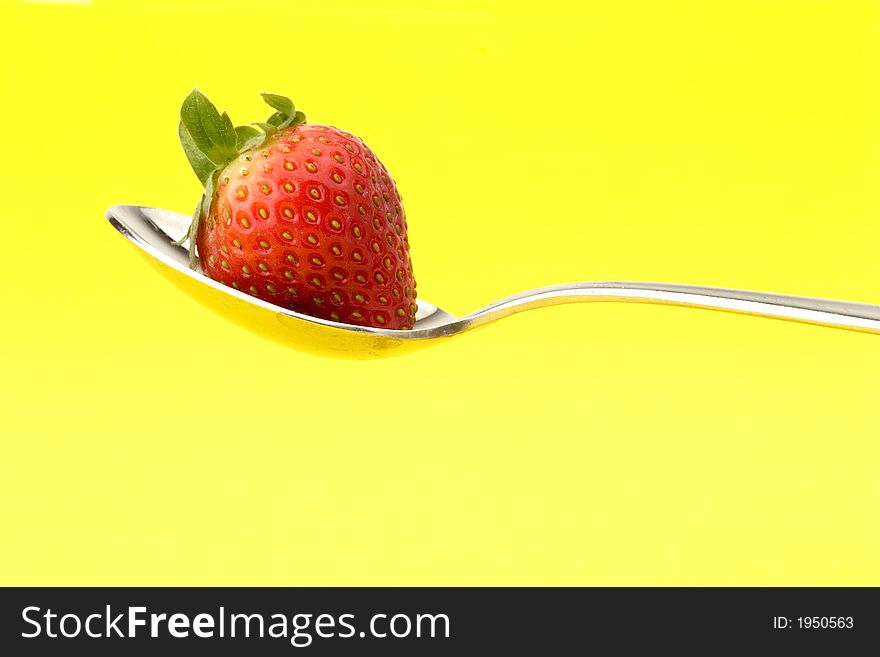 Strawberry on a spoon on yellow background