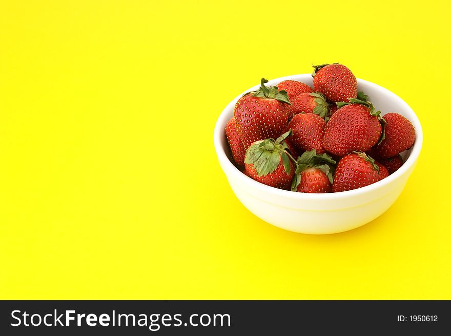 Bowl of ripe strawberries in a white bowl on yellow background. Bowl of ripe strawberries in a white bowl on yellow background