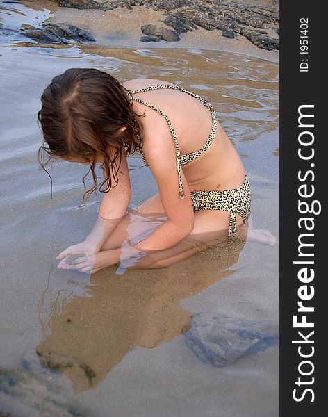 A girl is looking for crabs in the sand of ocean water pond. A girl is looking for crabs in the sand of ocean water pond