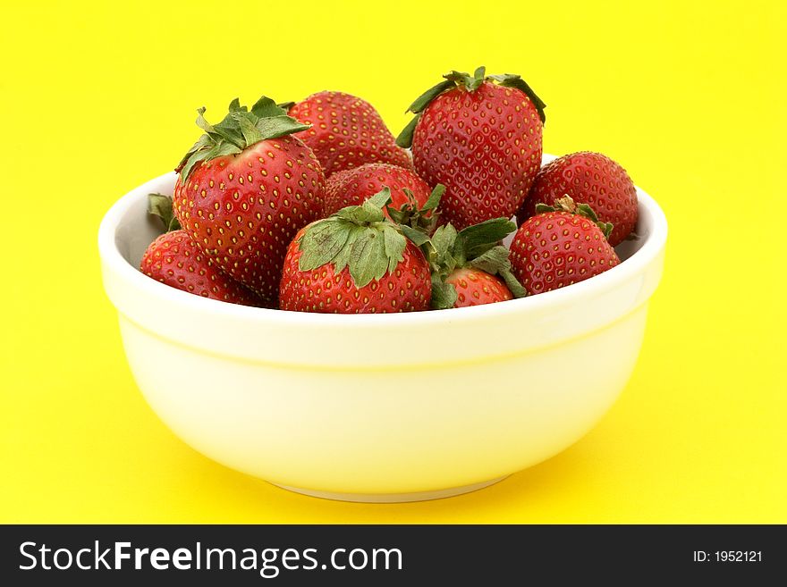 Bowl of ripe strawberries in a white bowl on yellow background. Bowl of ripe strawberries in a white bowl on yellow background