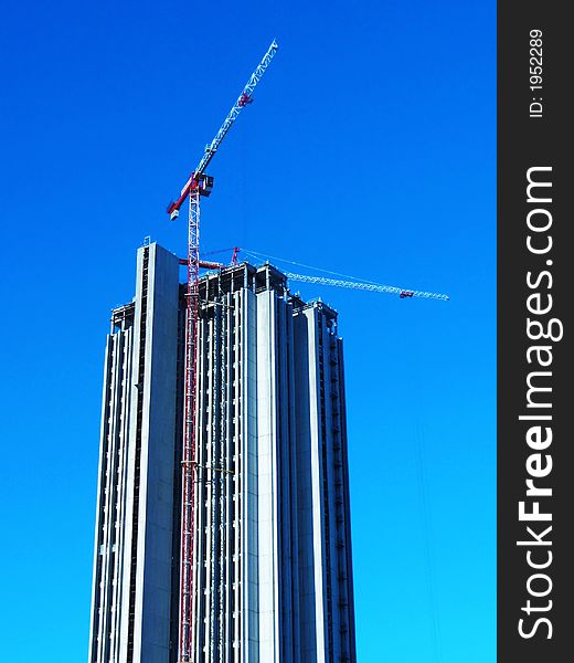 Two hoisting cranes building skyscraper office block in bright blue sky. Two hoisting cranes building skyscraper office block in bright blue sky