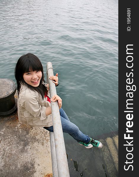 Asian girl smiling holding onto railing with legs hanging. Asian girl smiling holding onto railing with legs hanging