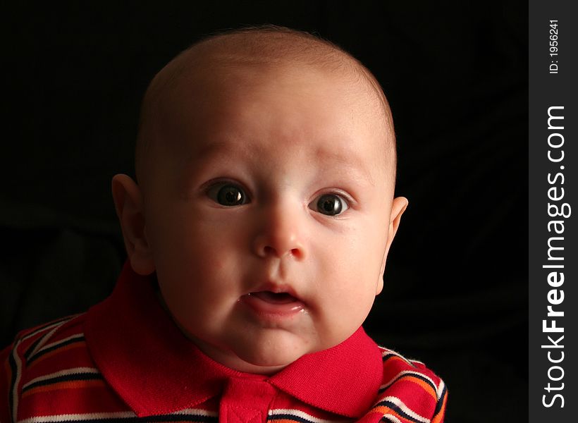 The face of a baby boy posing for the camera on a black background. The face of a baby boy posing for the camera on a black background.