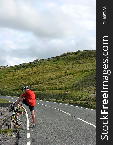 Male cyclist stopping for a rest on an uphill rural mountain road. Male cyclist stopping for a rest on an uphill rural mountain road.