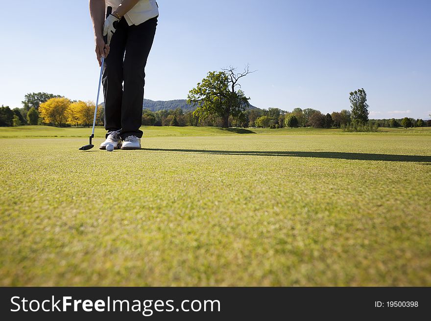 Active senior female golf player putting golf ball on green on beautiful golf course with blue sky in background. Active senior female golf player putting golf ball on green on beautiful golf course with blue sky in background.