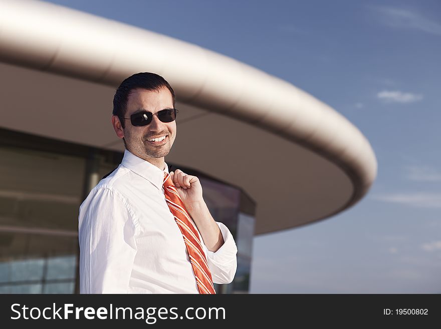 Portrait of smiling young business person in white shirt, orange tie and sunglasses standing in front of office building. Portrait of smiling young business person in white shirt, orange tie and sunglasses standing in front of office building.