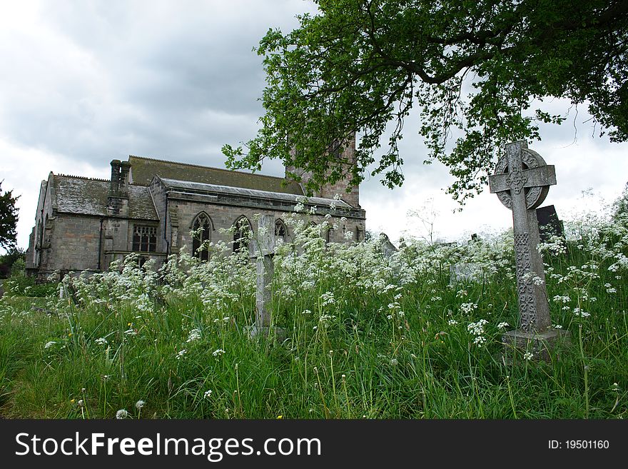 A churchyard in Ellastone, Staffordshire England showing wild flowers and grave stones with dark skyes and church. A churchyard in Ellastone, Staffordshire England showing wild flowers and grave stones with dark skyes and church.