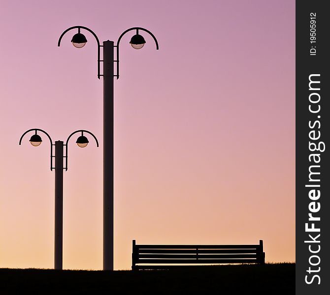 Silhouette of empty bench and streetlamps against a beautiful evening pink sky. Silhouette of empty bench and streetlamps against a beautiful evening pink sky
