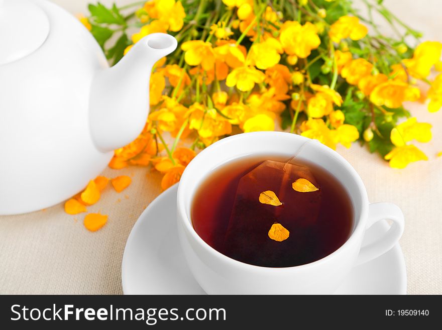 White cup of tea and buttercup flowers, on the table