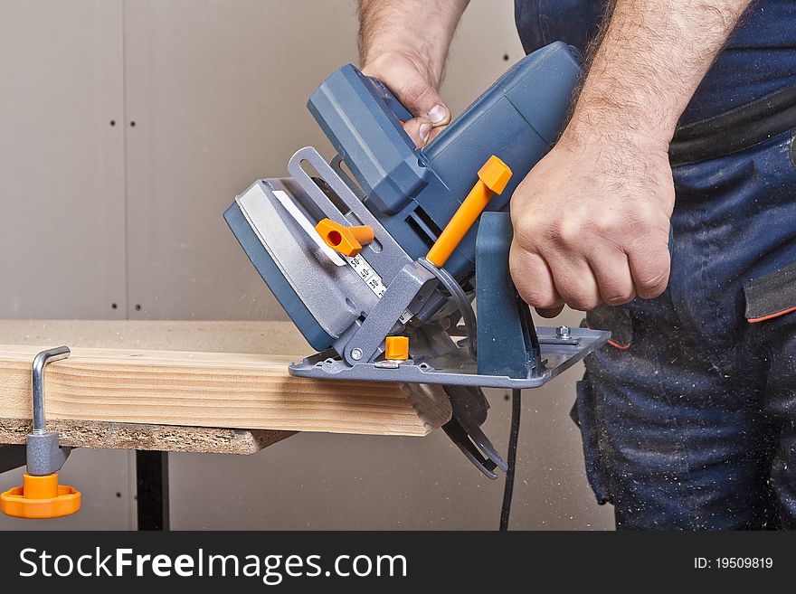 Close-up of a construction worker's hand and power tool while planing a piece of wood trim for a project. Close-up of a construction worker's hand and power tool while planing a piece of wood trim for a project.