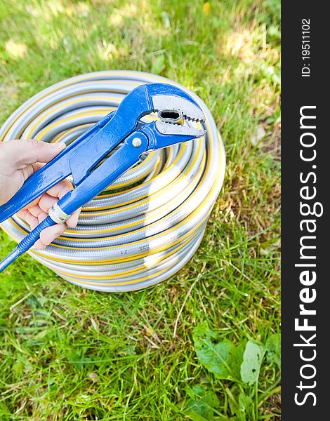 Blue metall spanner and plastic hose on green grass in summer