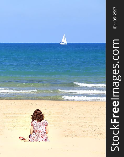 Girl sitting on a sandy beach and looking at a small white sail in the blue sea. Girl sitting on a sandy beach and looking at a small white sail in the blue sea