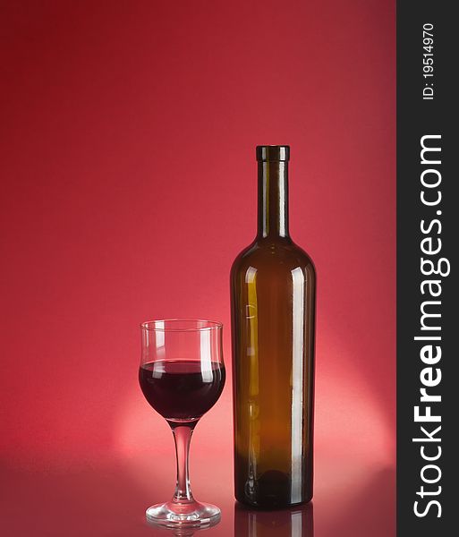 Glass and bottle of red wine over dark red background