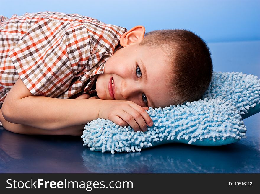 Cute boy resting on a pillow against blue background