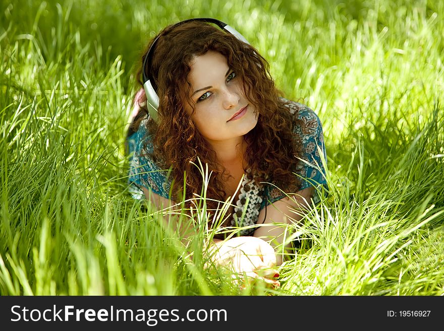 Redhead girl with headphone at green grass