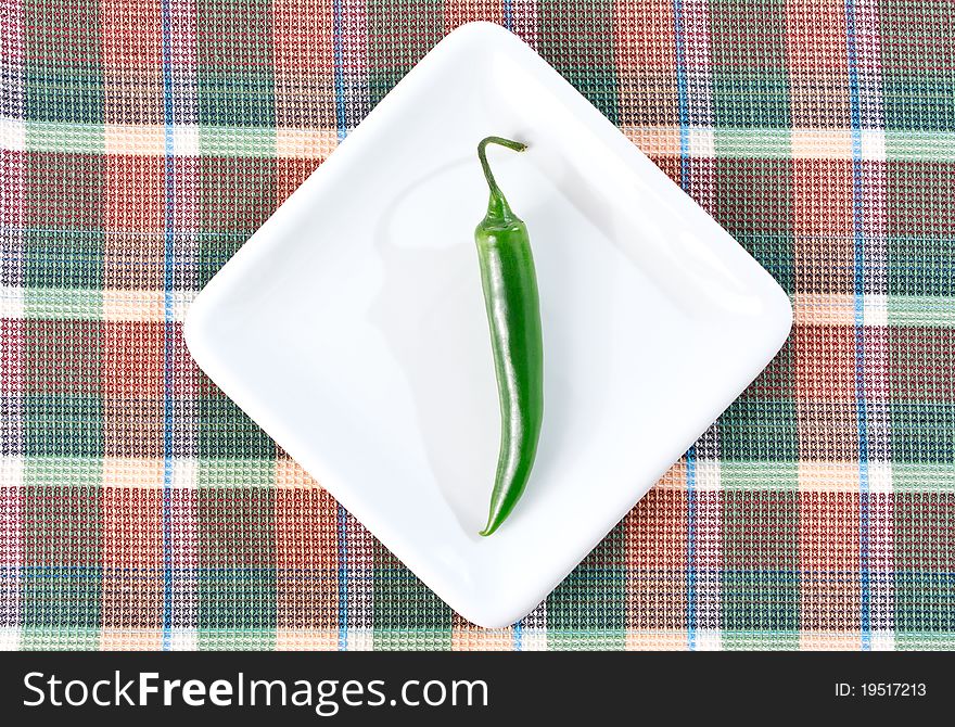 One green chili pepper on a white plate and checkered placemat