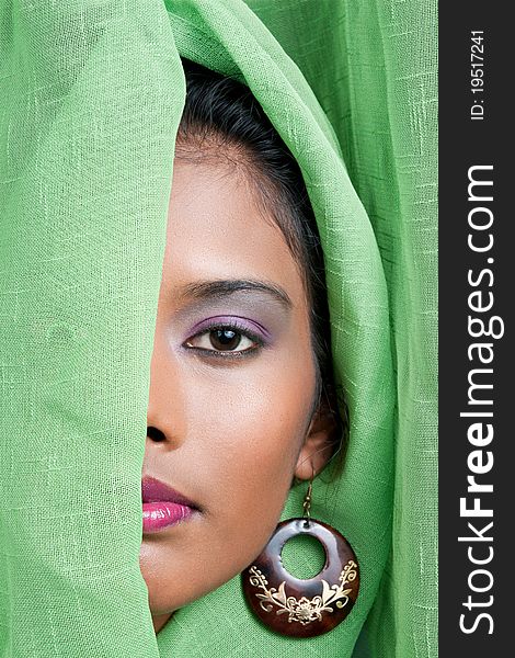 Beautiful woman of east indian descent looks from behind a green curtain. Beautiful woman of east indian descent looks from behind a green curtain