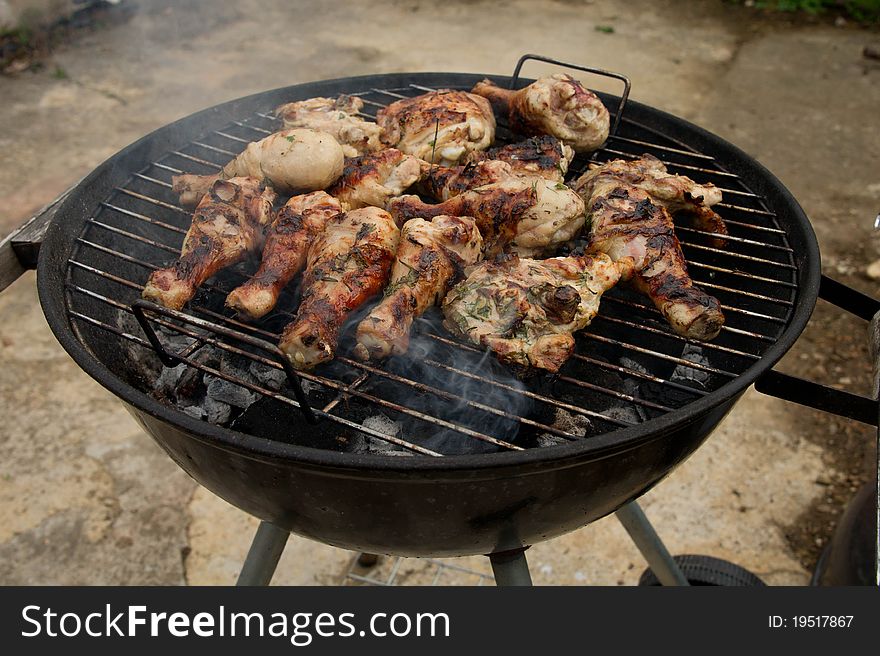 Barbecuing chicken drumsticks marinated in herbs