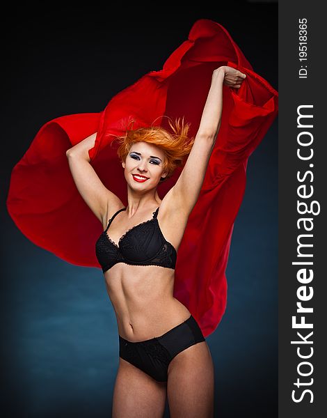 Woman with short red hair and black underwear holding fluttering red scarf with both hands up to wind. Woman with short red hair and black underwear holding fluttering red scarf with both hands up to wind.