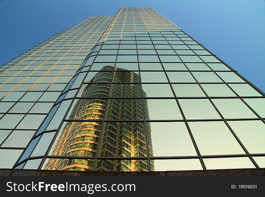 A Sky Scraper Has Another Building Clearly Reflected oOn Its Many Glass Panes. Also Features a Beautiful Blue Sky. A Sky Scraper Has Another Building Clearly Reflected oOn Its Many Glass Panes. Also Features a Beautiful Blue Sky