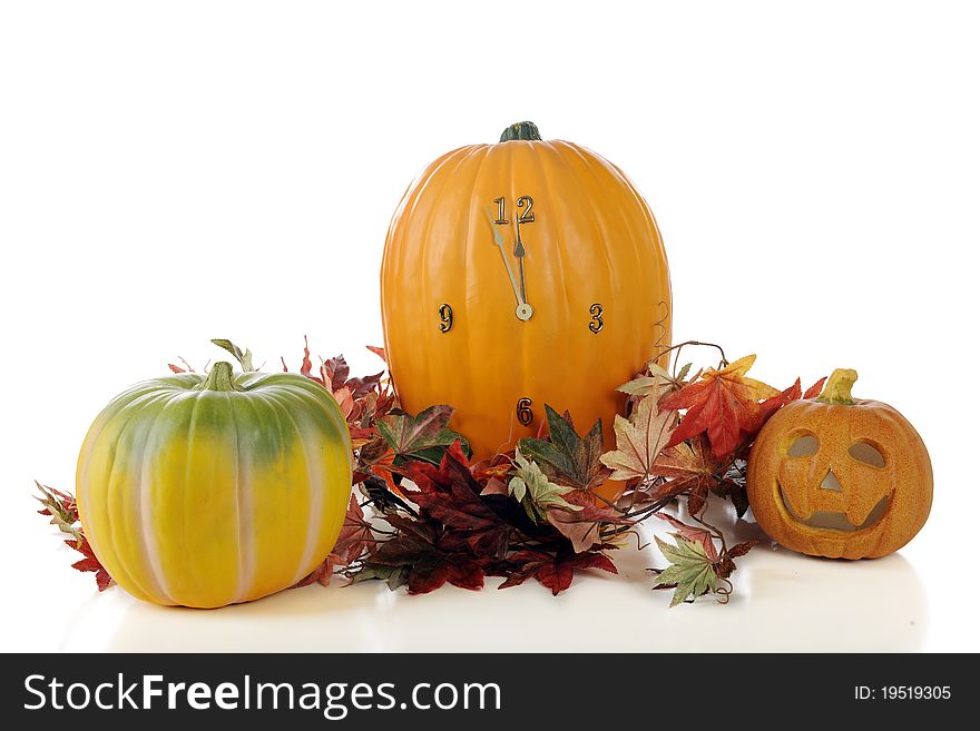 A still life composed of pumpkins, a jack-o-lantern and colorful leaves, with a clock imbedded in the central pumpkin.  The time reads 11:57.  Isolated on white. A still life composed of pumpkins, a jack-o-lantern and colorful leaves, with a clock imbedded in the central pumpkin.  The time reads 11:57.  Isolated on white.